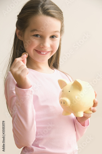 Photo: Caucasian girl putting coin into piggy bank Caucasian girl putting coin into piggy bank