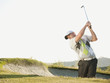 Caucasian golfer hitting ball out of bunker