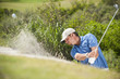 Caucasian golfer hitting ball out of bunker