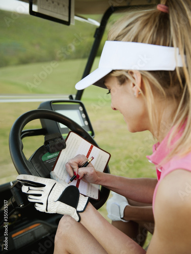 Photo: Caucasian woman in golf cart writing on score card Caucasian woman in golf cart writing on score card