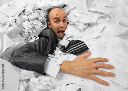 Photo: Businessman sinking in heap of documents Businessman sinking in heap of documents