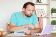 Worried man calculating bills by the table at home