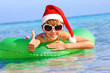 Child in santa hat  floating on inflatable ring in sea.