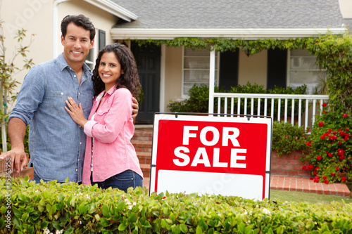 Photo: Hispanic couple outside home with for sale sign Hispanic couple outside home with for sale sign