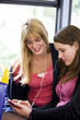 Two teenage girls sitting on a bus, listening to music