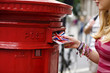 A teenage girl putting postcards into a red letterbox
