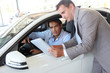 Car seller with car buyer looking at electronic tablet