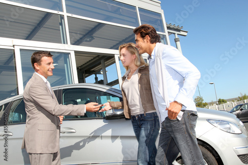 Photo: Car seller with couple outside car dealership Car seller with couple outside car dealership