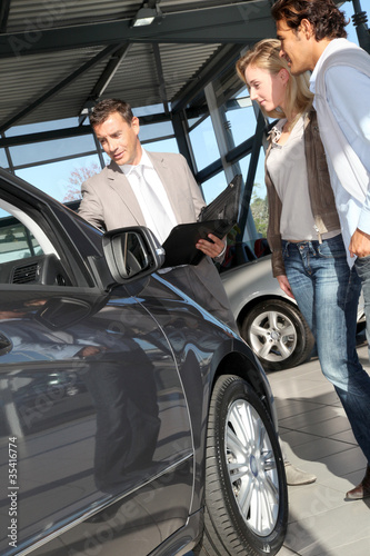 Photo: Car seller with couple in showroom Car seller with couple in showroom