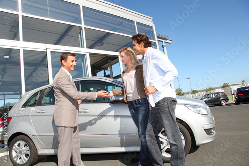 Photo: Car seller with couple outside car dealership Car seller with couple outside car dealership