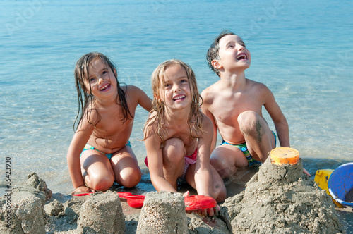 Photo: Three kids making sand castle by the sea Three kids making sand castle by the sea