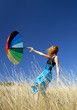 Redhead girl with umbrella at windy grass meadow.
