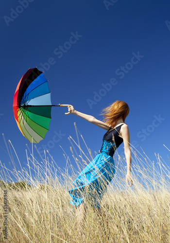 Photo: Redhead girl with umbrella at windy grass meadow. Redhead girl with umbrella at windy grass meadow.