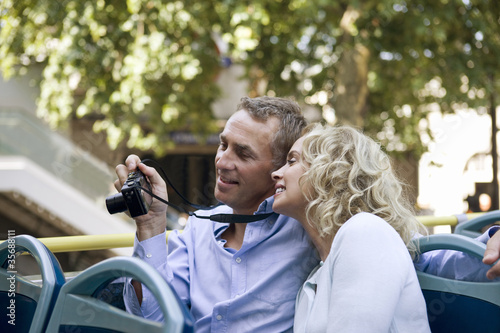 Photo: A couple sitting on a sightseeing bus, holding a camera A couple sitting on a sightseeing bus, holding a camera