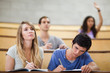 Students taking notes while their classmate is raising her hand