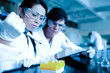 Cute scientist dropping liquid in test tubes while her partner i