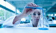 Scientist pouring a liquid in an Erlenmeyer flask with a test tu