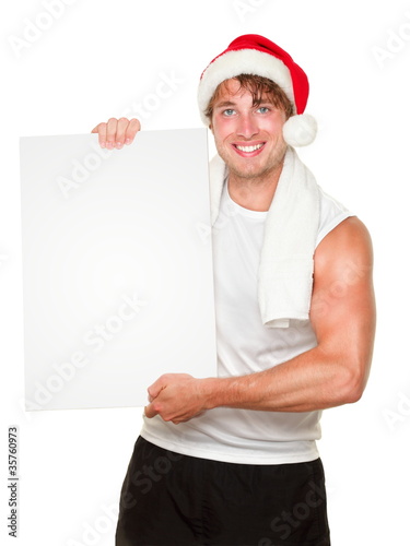 Photo: Fitness man holding sign wearing christmas santa hat Fitness man holding sign wearing christmas santa hat