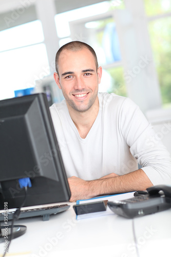 Photo: Smiling office worker sitting in front of desktop computer Smiling office worker sitting in front of desktop computer
