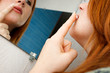 Photo: Red head girl applying white cream to her lip in a mirror Red head girl applying white cream to her lip in a mirror