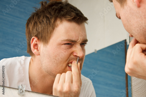 Photo: Young man using tweezers to pull nostril hair Young man using tweezers to pull nostril hair