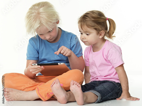 Photo: Cute girlfriends sitting on the floor and playing with touchpad Cute girlfriends sitting on the floor and playing with touchpad