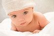 Little baby lying on the blanket and is wearing a white hat.