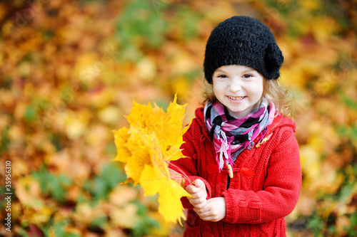 Foto: Little girl in a red coat at autumn holding leaves Little girl in a red coat at autumn holding leaves