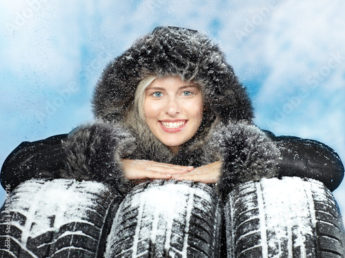 Photo: Beautiful woman with winter coat behind snowy winter tyres Beautiful woman with winter coat behind snowy winter tyres