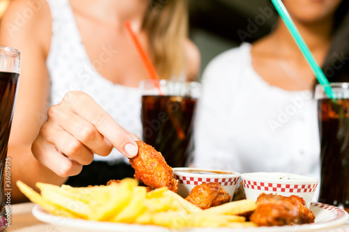 Foto: Zwei Frauen essen Chicken wings und trinken Cola Zwei Frauen essen Chicken wings und trinken Cola