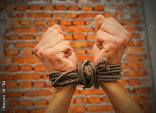 Photo: Hands tied up with rope against brick wall Hands tied up with rope against brick wall
