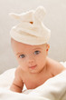 Little baby lying on the blanket and is wearing a white hat.