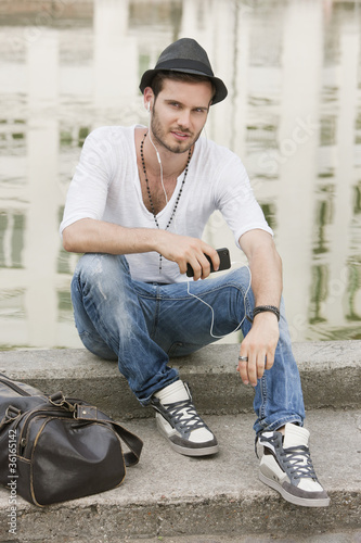 Foto: Man sitting on the ledge of a canal and listening to music with an MP3 player, Paris, Ile-de-France, France Man sitting on the ledge of a canal and listening to music with an MP3 player, Paris, Ile-de-France, France