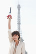 Foto: Woman holding a replica of the Eiffel Tower in front of the original one, Paris, Ile-de-France, France Woman holding a replica of the Eiffel Tower in front of the original one, Paris, Ile-de-France, France