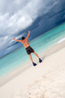 Tanned man jump in blue flippers on sand beach and ocean Tanned man jump in blue flippers on sand beach and ocean