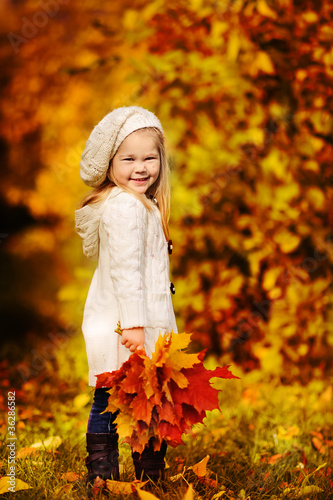 Photo: little girl in warm cardigan smiling against the background of f little girl in warm cardigan smiling against the background of f