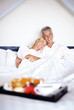 Portrait of mature couple on bed with breakfast in front