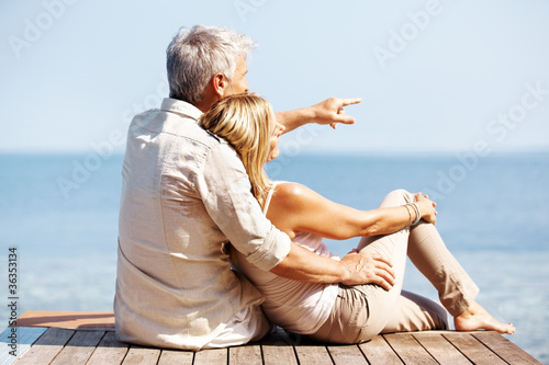 Photo: Rear view of man sitting on wooden pier with his wife Rear view of man sitting on wooden pier with his wife