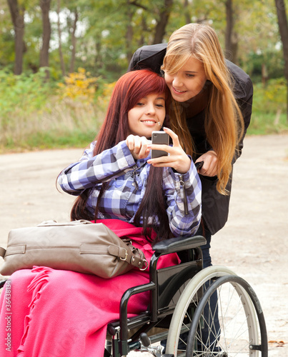 Photo: invalid girl on the wheelchair with friend outdoors invalid girl on the wheelchair with friend outdoors