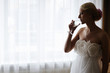 Silhouette of a bride drinking wine in front of a window