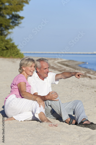 Photo: Happy Senior Couple Sitting Pointing on Beach Happy Senior Couple Sitting Pointing on Beach