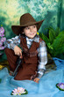 cute little boy dressed as a cowboy with a gun on a green backgr