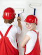 Two young worker having fun while painting a white wall