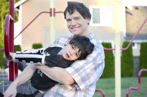Photo: Father helping disabled son to play at playground Father helping disabled son to play at playground
