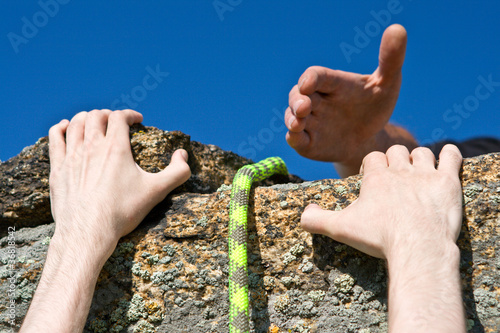 Photo: Rock climber reaching for helping-hand partner. Rock climber reaching for helping-hand partner.