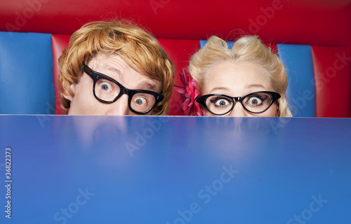 Foto: Nerdy couple hiding behind a table Nerdy couple hiding behind a table