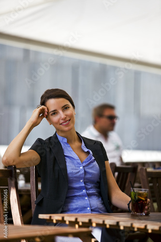 Photo: Pretty young woman sitting in garden of a restaurant Pretty young woman sitting in garden of a restaurant