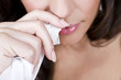 A young woman wiping her nose with a tissue, close-up