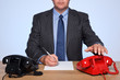 Businessman sat at desk with two telephones.