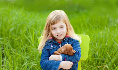 Photo: Blond kid girl with puppy pet dog in green grass Blond kid girl with puppy pet dog in green grass